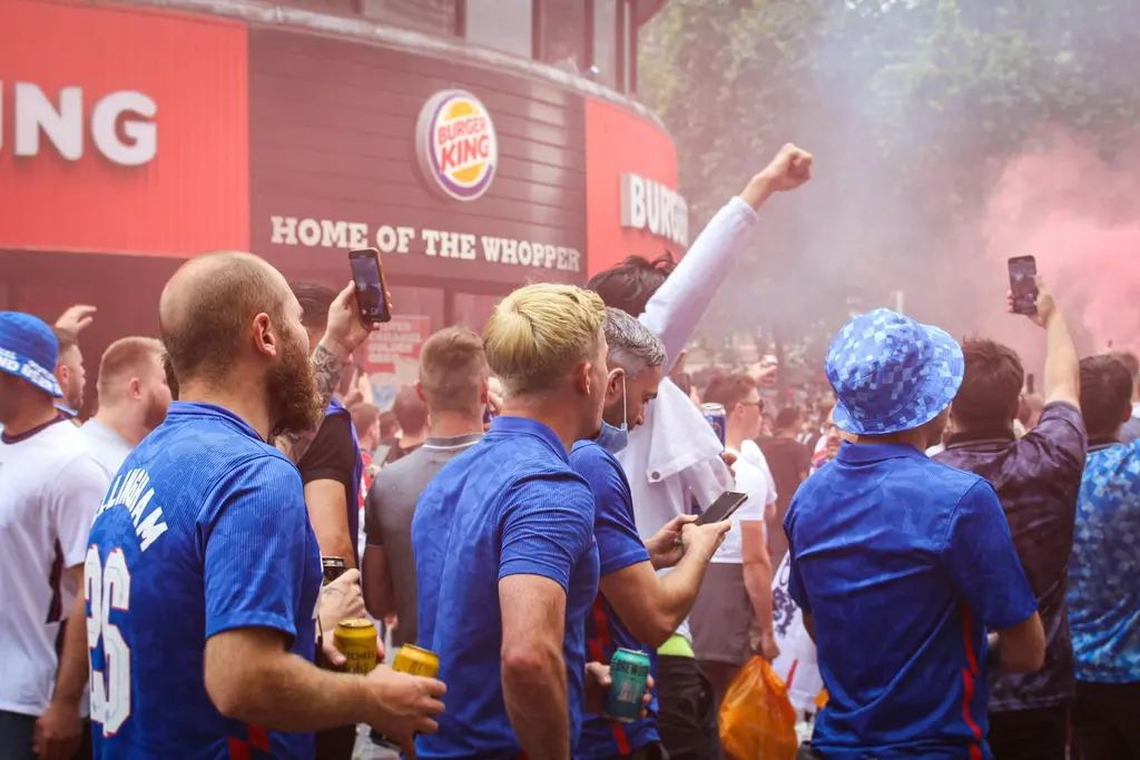 Fans celebrating at an outdoor World Cup watch party, throwing coloured powder in the air at a FIFA Fan Festival