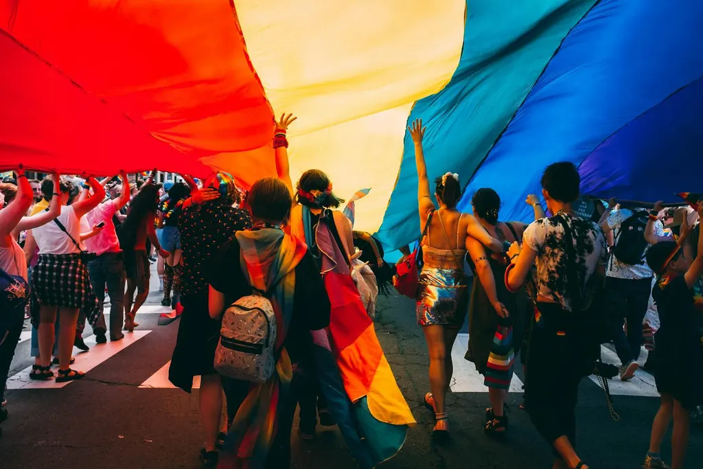 Crowd marching together under a large rainbow flag during the Boston Pride parade through Back Bay