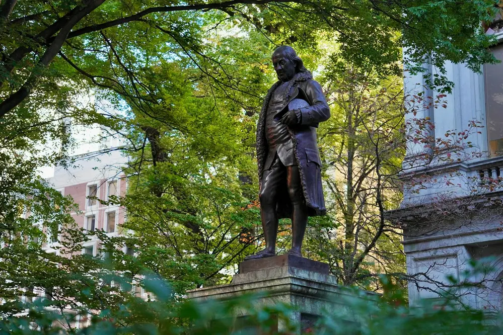 Bronze statue of Benjamin Franklin surrounded by trees near the Freedom Trail in Boston