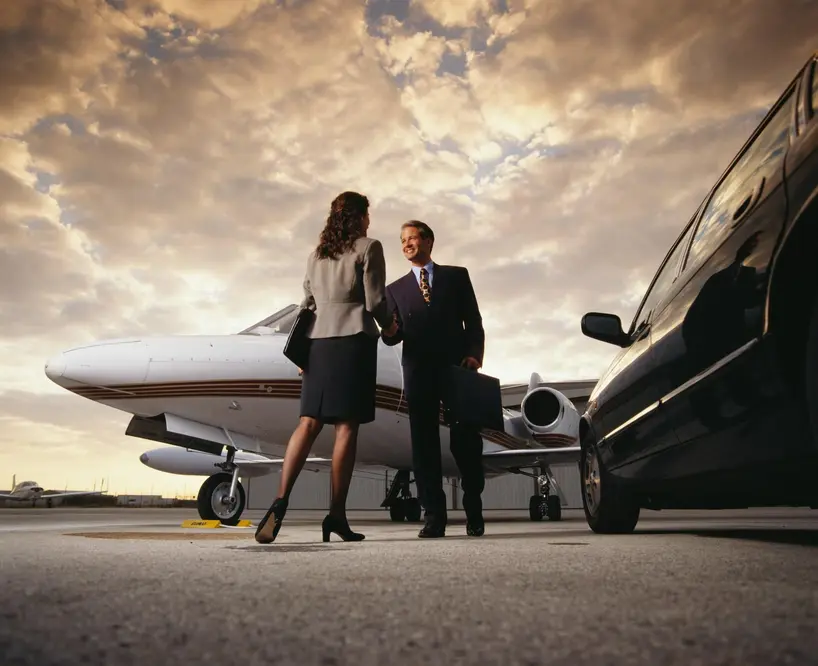 Business travelers greeting each other beside a private jet and a luxury car on the airport tarmac